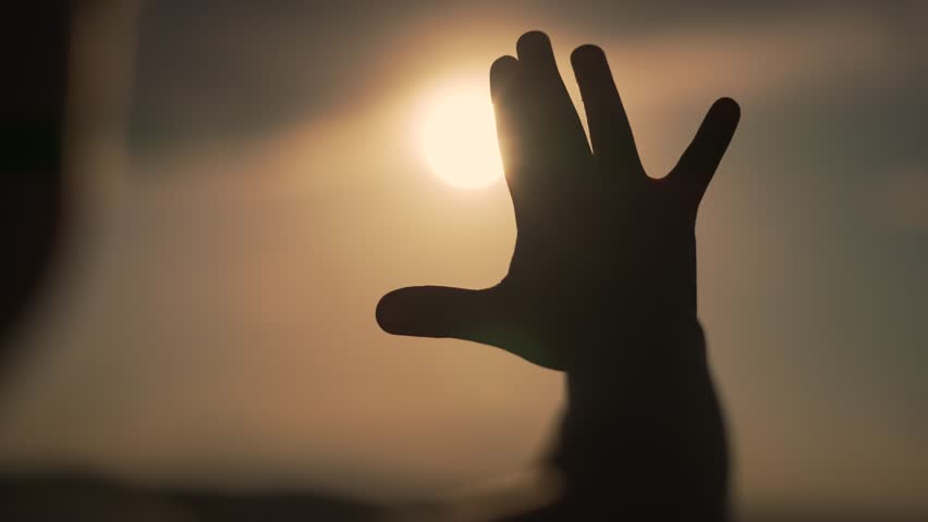 Silhouette of child at sunset. Palm reaching for the sun. Dreamy silhouette of palm against sunset. Cinematic moment silhouette. Sunset creates silhouette of child palm. Reaching palm dream concept.