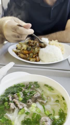 Vietnamese transparent soup with rice noodles, meat and greens in white bowl. Steaming hot transparent broth with rice pasta and various additives