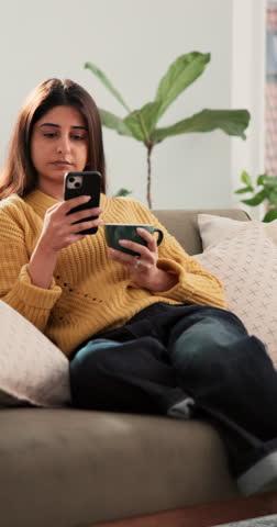 Coffee, phone and thinking with woman on sofa in living room of home for break or contemplation. Beverage, relax and vision with Indian person typing text message in apartment for morning me time