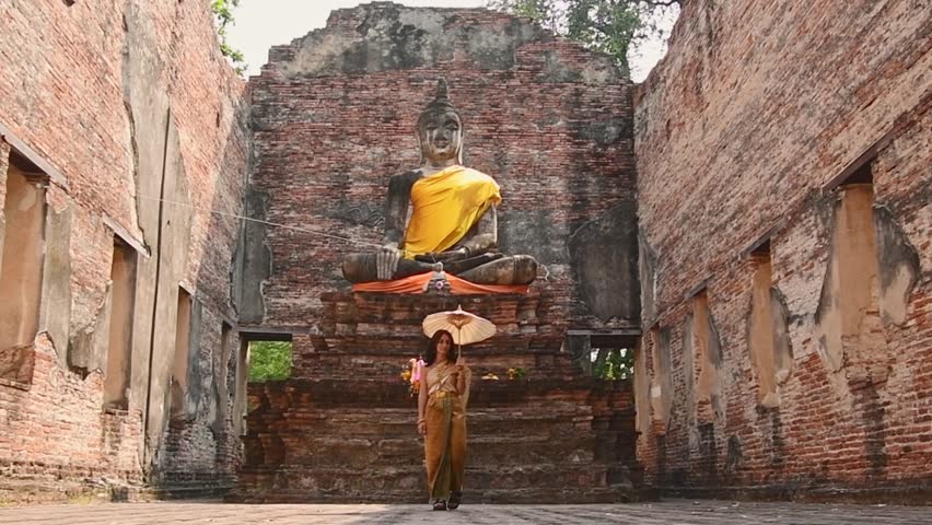 Thailand, Ayutthaya - march 15th, 2023: Woman in traditional Thai dress holding umbrella sightseeing visit ancient Buddha statue.Ayutthaya historical park. Concept heritage, spirituality, thai culture