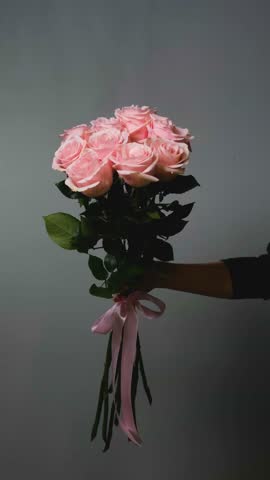A florist creates a custom bouquet. Close-up of a bouquet of roses against a gray background. Beautiful pink roses at a flower shop.