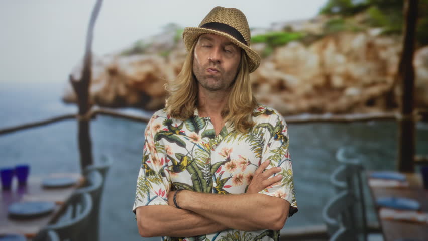 Man with crossed arms and straw hat wearing floral shirt on seaside restaurant terrace overlooking rocky coast; rejection.
