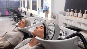 Two women relaxing with their eyes closed during a hair steam treatment at a modern hairdressing salon. Professional spa procedure - Powered by Shutterstock - Get 15% off with code: PIKWIZARD15