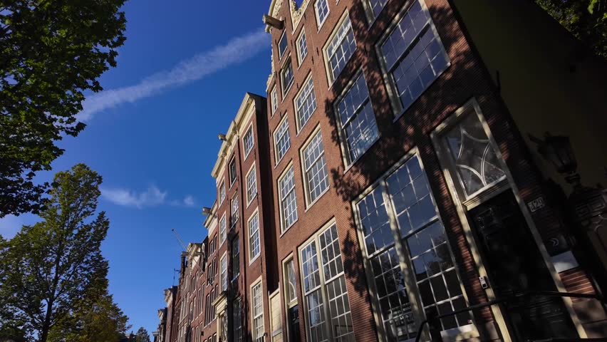 Upward view of Amsterdam canal houses with large windows and blue sky reflections on a sunny morning. Location: Amsterdam, Noord-Holland, Netherlands (Amsterdam, Noord-Holland, Nederland).
