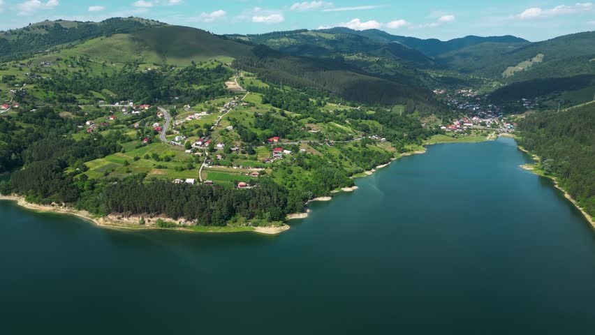 Aerial drone view of Lake Bicaz in Romania, surrounded by green hills and mountains. Peaceful nature and scenic landscape in summer. Drone panning left.