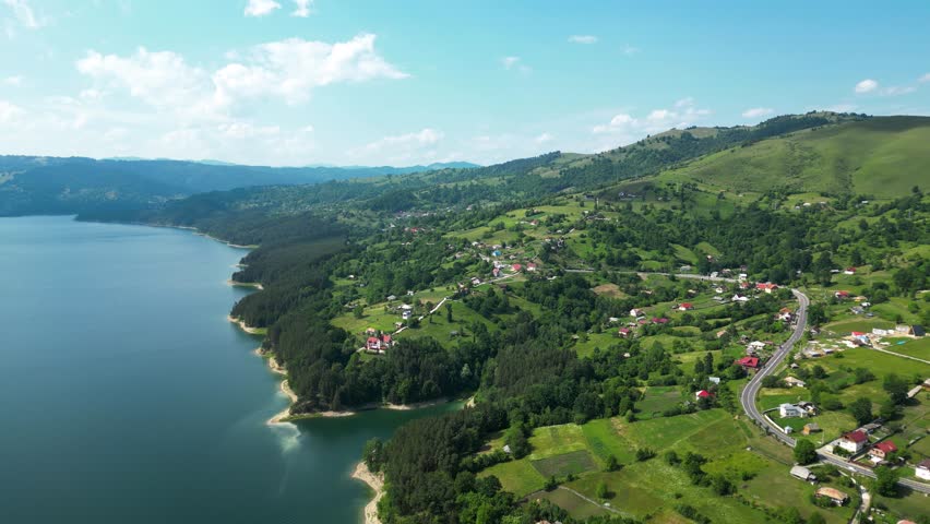 A breathtaking aerial view of Lake Bicaz surrounded by lush green hills and serene countryside, showcasing the natural beauty and peaceful landscapes of Romania. Drone panning right.