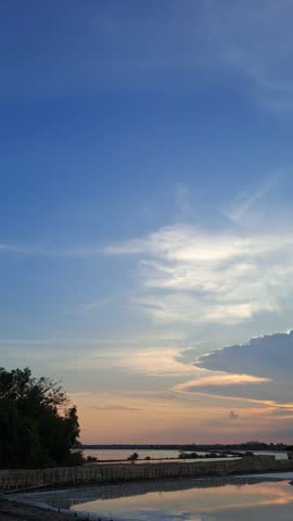 Peaceful sunset over a traditional salt farm, glowing in warm orange and red hues, with calm reflections and beautiful clouds painting the serene evening sky.