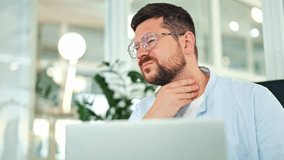 Unwell male in a light blue shirt and glasses experiences throat pain and discomfort while sitting at a laptop in a modern office, feeling ill and suffering. - Powered by Shutterstock - Get 15% off with code: PIKWIZARD15