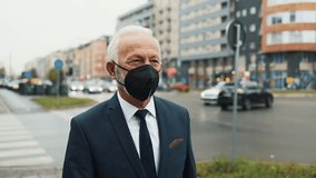 Successful senior businessman wearing a protective face mask walking on a city street and answering a phone call during the coronavirus pandemic, with urban traffic in the background - Powered by Shutterstock - Get 15% off with code: PIKWIZARD15