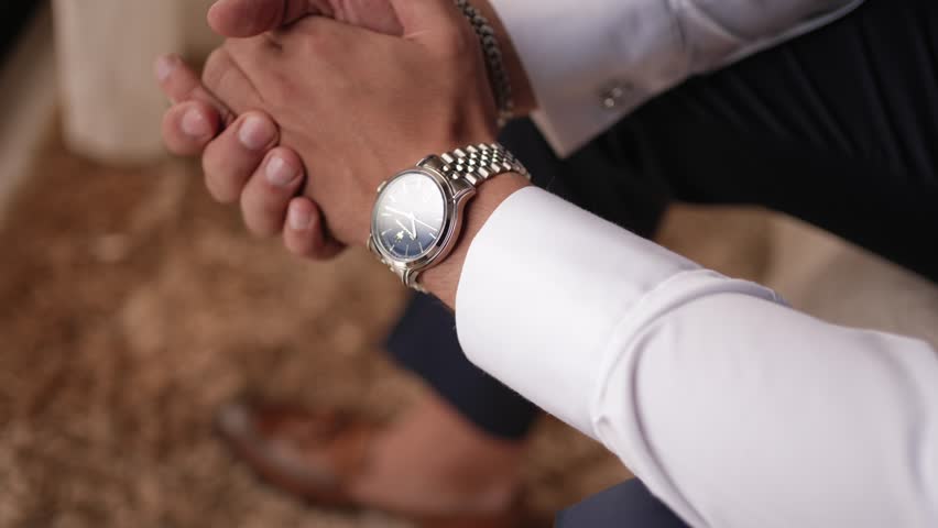 Closeup of groom wearing wristwatch and white shirt before wedding