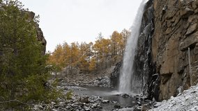A powerful waterfall thunders down a sheer rock face into a pool in the remote Mongolian wilderness. The raw, rugged landscape is dotted with golden larches and early winter snow. - Powered by Shutterstock - Get 15% off with code: PIKWIZARD15