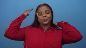 Woman wearing red blouse adjusts her hair and straightens eyeglasses in studio with bright blue wall behind her; confidence. - Powered by Shutterstock - Get 15% off with code: PIKWIZARD15