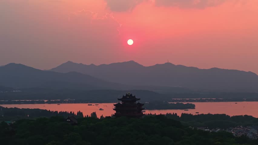 Aerial view of Chenghuang pagoda at sunset over Xihu lake in Hangzhou featuring mountains and lush green trees