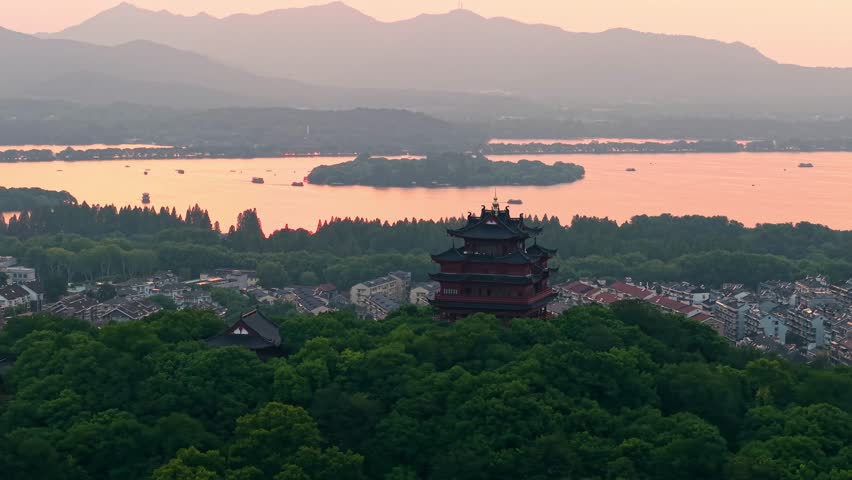 Aerial view of Chenghuang pagoda at sunset over Xihu lake in Hangzhou featuring mountains and lush green trees