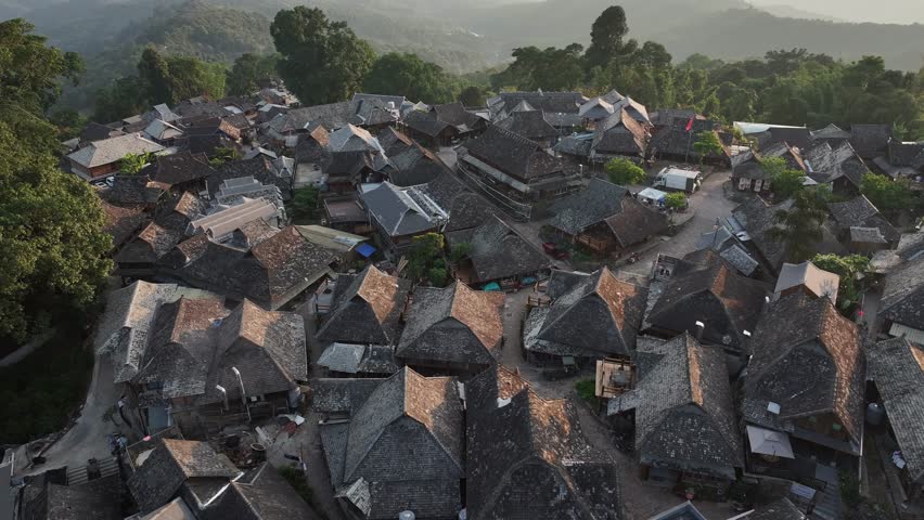 Aerial view of clustered rooftops and winding pathways of Wengji Village, nestled amidst lush greenery and rolling hills in Jingmaishan, Yunnan, China.
