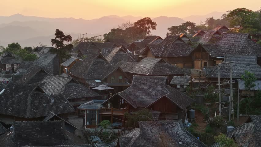 Aerial view of clustered rooftops, showcasing a dense village nestled amongst rolling hills in warm light, Wengji Village, Yunnan, China.