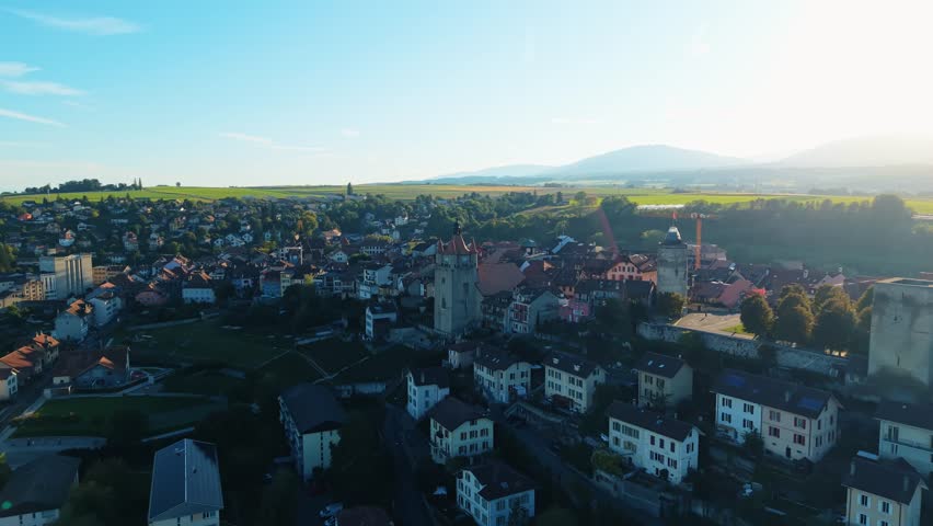 Aerial view of Orbe cityscape shows towers, houses and green fields under a clear sky, creating a serene and picturesque scene, Orbe, Vaud, Switzerland.