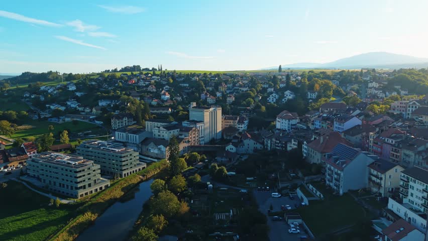 Aerial view of the radiant Orbe cityscape featuring buildings and a flowing river, bathed in the warm glow of the sunset, Orbe, Vaud, Switzerland.