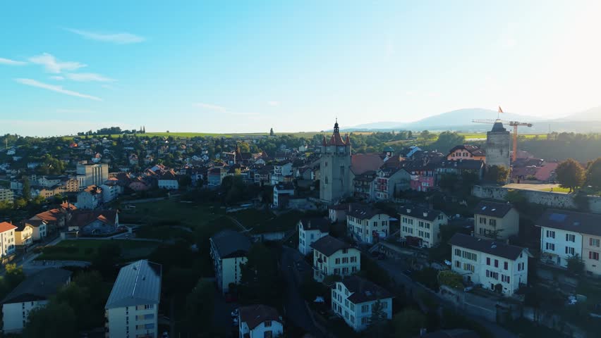 Aerial view of Orbe cityscape at sunset, a symphony of warm light over buildings and lush landscapes, creating an idyllic scene, Orbe, Vaud, Switzerland.