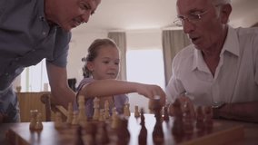 Joyful multi generational family playing a chess board game at home, with the grandfather teaching his granddaughter strategy while the proud father watches and smiles with amusement - Powered by Shutterstock - Get 15% off with code: PIKWIZARD15