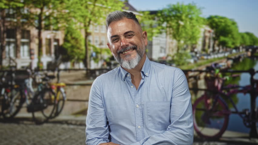 Man extends hand toward camera beside parked bicycles on amsterdam street while smiling and beckoning; welcoming invitation.