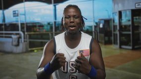 Young man smiling with clenched fists, wearing usa basketball jersey with flag patch and blue wristbands, dreadlocks visible, standing at airport terminal entrance; pride celebration. - Powered by Shutterstock - Get 15% off with code: PIKWIZARD15