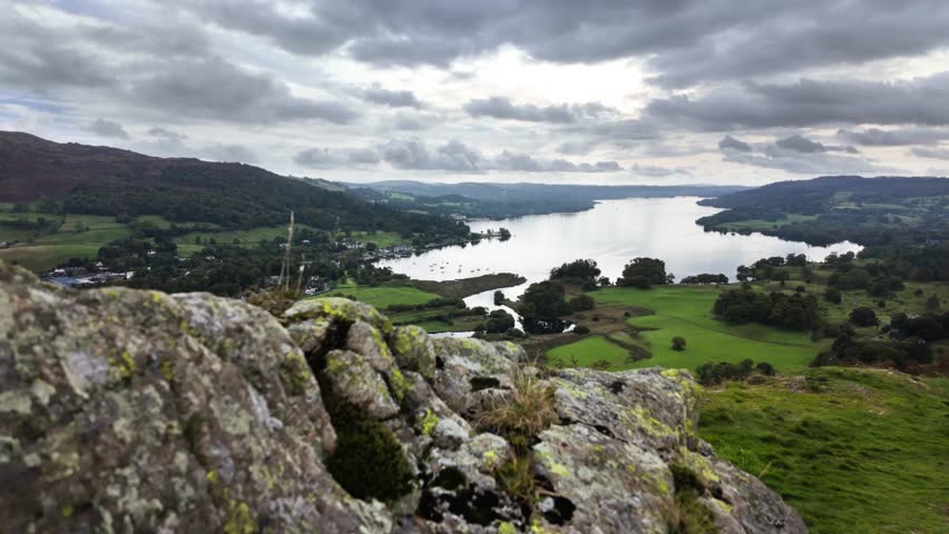 Moving over rocks on a hilltop to reveal Lake Windermere in the distance. Lake District, UK