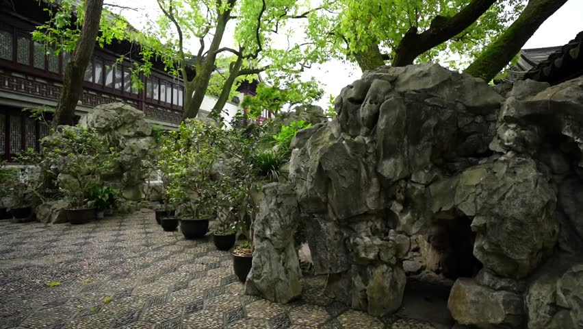 Panning left reveals a female photographer in a pink raincoat taking pictures inside Yuyuan Garden. Shanghai, China