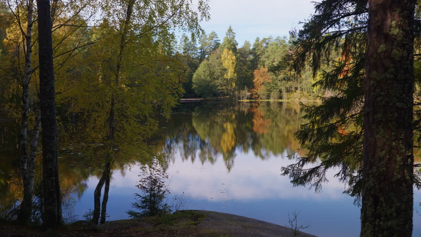Wide shot of an opening in the forest showing a scenic view of a lake with colorful trees