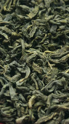 Vertical rotating close up of dried green tea leaves, rich organic texture and curled shapes, fresh ingredient for healthy lifestyle