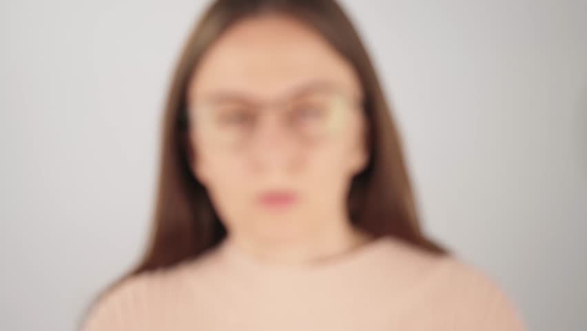 Blurred view of a tired woman taking off her eyeglasses and rubbing her eyes from digital eye strain and fatigue. Concept of poor eyesight, vision problems and overworked eyes.