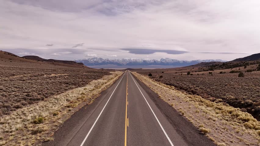 Aerial view of the Lincoln Highway road cutting through the arid landscape towards snow-capped mountains in the distance, Austin, Nevada, United States.