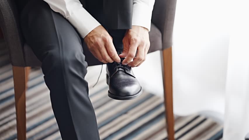 Man ties shoelaces on formal shoes in a bright room