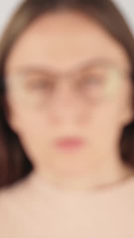 Vertical close-up of a blurred view of a tired woman taking off her eyeglasses and rubbing her eyes from digital eye strain and fatigue. Concept of poor eyesight, vision problems and overworked eyes.