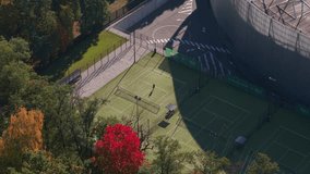 Aerial view of a tennis player serving on an outdoor court near a stadium in Kaunas, Lithuania, surrounded by autumn trees and urban infrastructure on a bright sunny day. - Powered by Shutterstock - Get 15% off with code: PIKWIZARD15