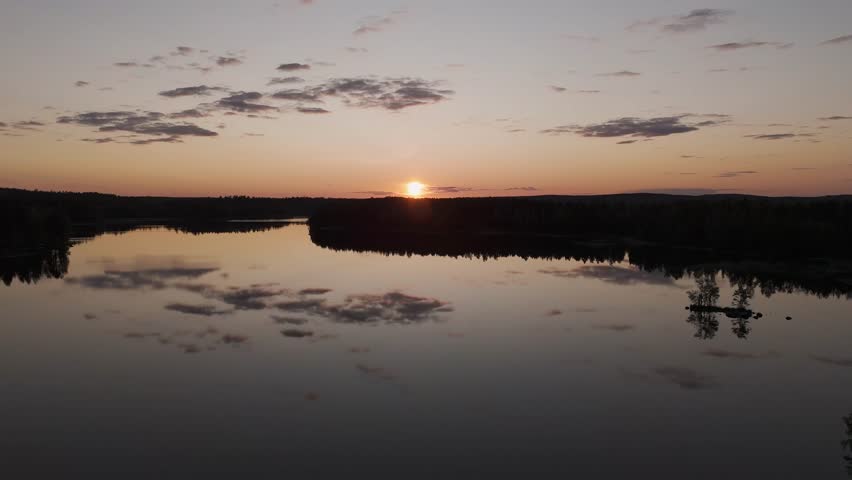Aerial view of a Finnish road at sunset winding between two lake shores in spring, where golden light reflects on the calm water creating a peaceful and poetic landscape