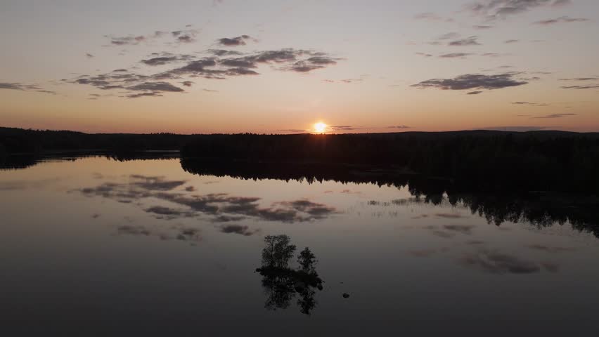 Aerial view of a Finnish road at sunset winding between two lake shores in spring, where golden light reflects on the calm water creating a peaceful and poetic landscape