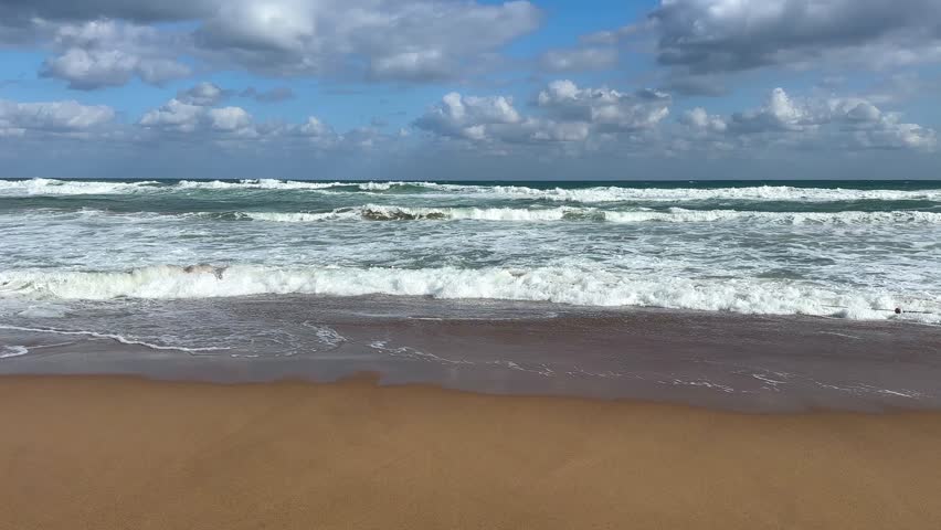 Shallow waves roll and crash on sandy beach in slow rhythm under blue sky