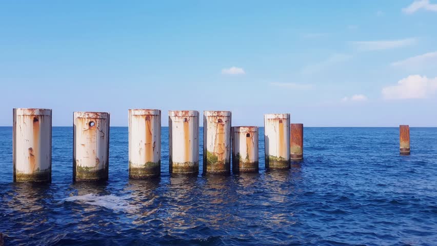 Seaside landscape of Baltic sea coast with calm waves rolling on huge metal piles forming shore protection dam construction under clear blue sky at summer day. No people seascape natural background.