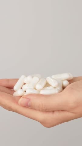 Vertical close-up of hand holding a pile of white capsules on a neutral background with copy space. Concept of dietary supplements, vitamins and healthcare pills.