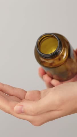 Close-up of a hand overloaded with white capsules while more are being poured from a bottle. Concept of excessive supplement use and uncontrolled self care routine.