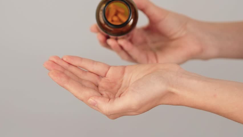 Close-up of a hand full of yellow capsules being poured from a bottle. Concept of vitamins, herbal supplements, turmeric curcumin, medication and daily healthcare routine.