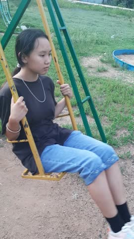 an Asian girl in a black T-shirt and blue jeans is riding an old yellow swing