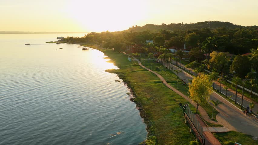 An aerial sunset view of lakeside promenade with boats, pathways, and green park along the shore