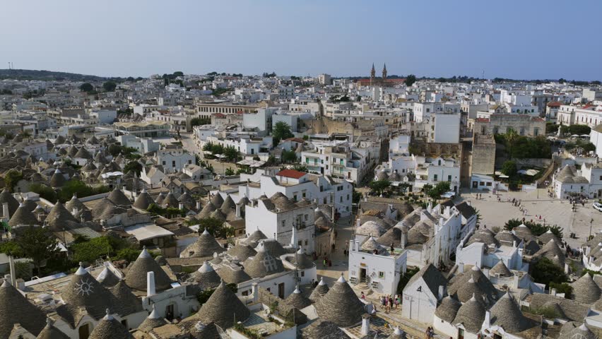 Alberobello cityscape in Puglia, Italy, featuring conical stone roofs and a historic town square. Aerial drone orbiting