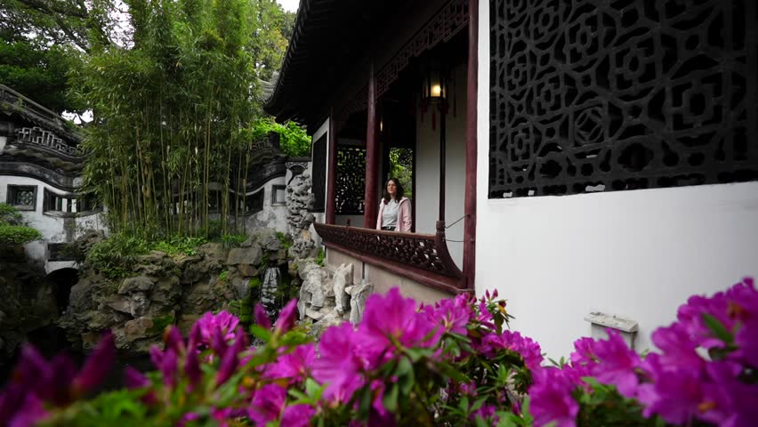 Slow motion of a tourist admiring lush vegetation from a balcony with purple flowers in foreground. Yuyuan Garden, Shanghai, China