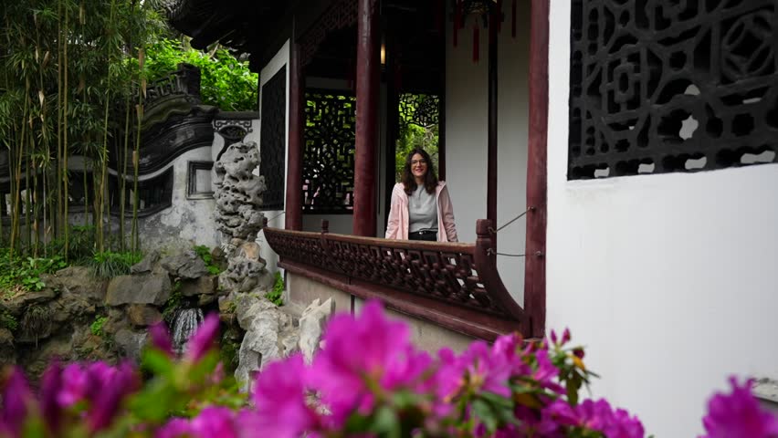 Slow motion of a woman smiling at camera while admiring the beauty of Yuyuan Garden from a balcony and purple flowers in foreground. Shanghai, China