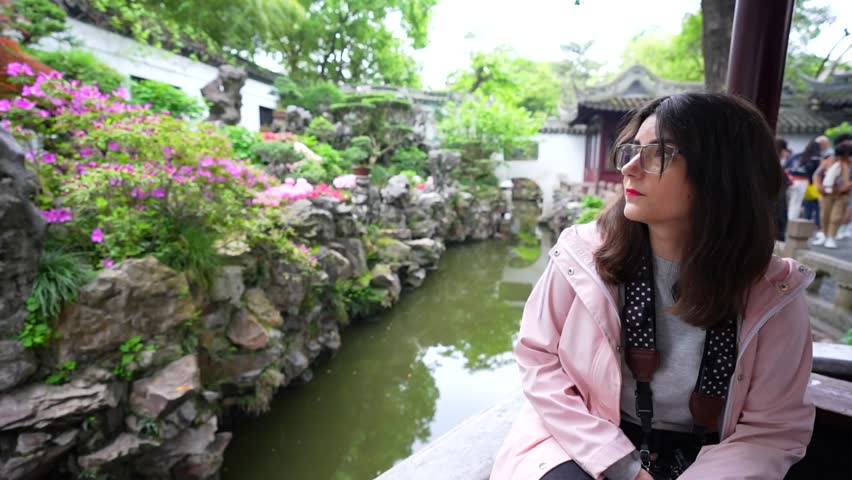 Caucasian woman sitting and admiring plants by a pond in Yuyuan Garden. Shanghai, China