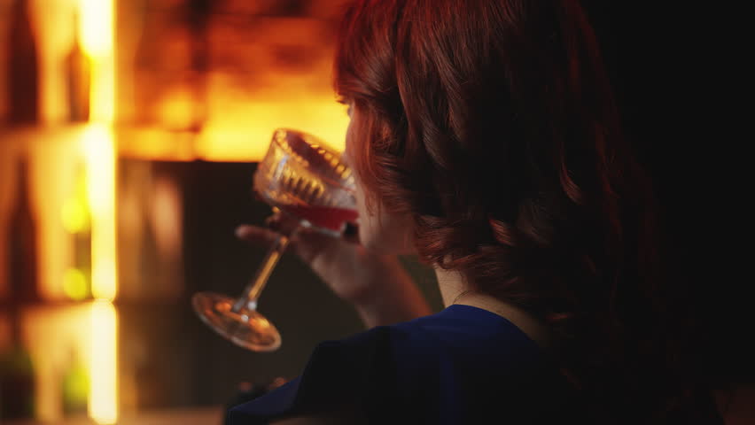 Redhead female drinking cocktail at bar counter, looking for date, close-up view