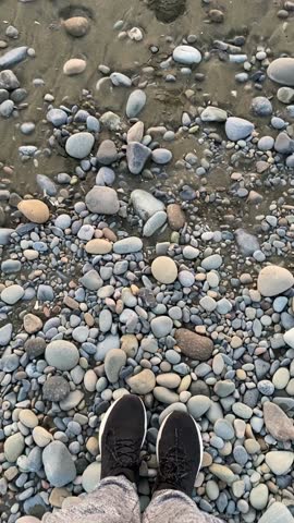 Pebbles scattered on sandy beach with persons foot visible, suitable for use as a background video